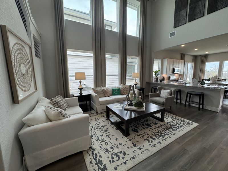 A spacious living room with high ceilings, large windows, neutral couches, and a cozy rug, flowing into a modern kitchen area. A spacious living room with high ceilings, large windows, neutral couches, and a cozy rug, flowing into a modern kitchen area.