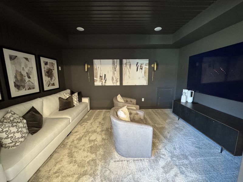 A cozy media room featuring a plush sofa, abstract art, soft lighting, and a large flat-screen TV for ultimate relaxation.