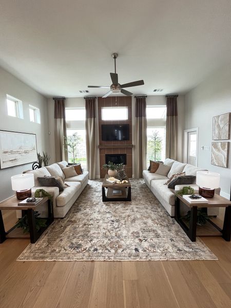 A spacious living room with plush sofas, elegant decor, a central fireplace, and a ceiling fan, exuding warmth and style.