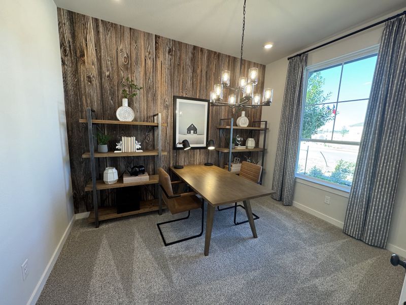 A chic home office with a rustic wood accent wall, modern chandelier, sleek desk, and stylish shelving.