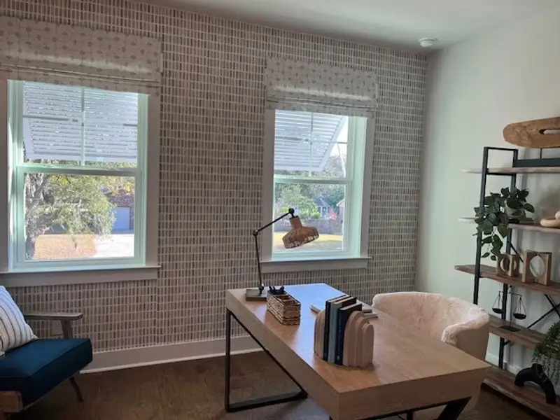 A cozy home office with patterned wallpaper, natural light, and a stylish desk featuring modern decor and shelving.