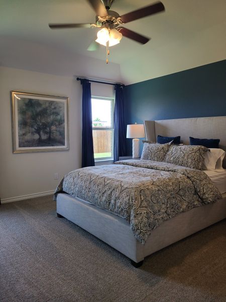 A cozy bedroom with a patterned comforter, dark accent wall, and ceiling fan, offering tranquility and style.