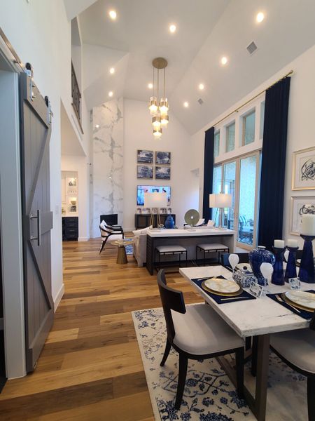 A spacious living area with high ceilings, chic lighting, and elegant dining set on hardwood floors.