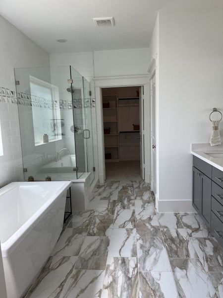 A luxurious bathroom featuring marble-tiled floors, a spacious glass shower, and a sleek gray vanity.