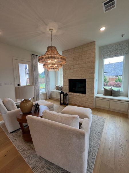 A cozy living room with plush seating, a stone fireplace, wooden floors, and a chic woven chandelier.