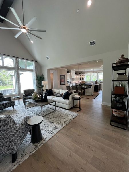 A spacious living area with modern furnishings, high ceilings, large windows, and an open layout leading to a chic kitchen.