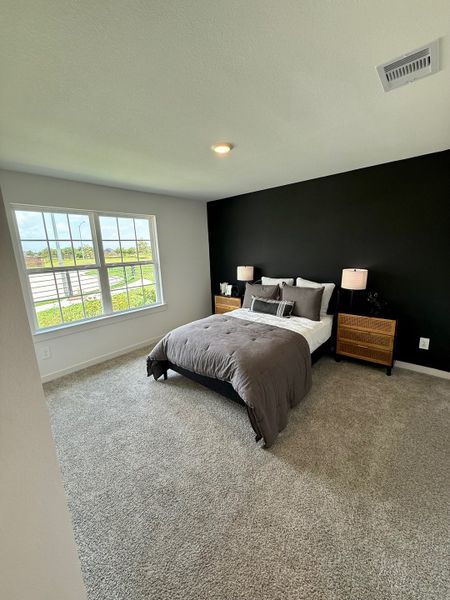 A cozy bedroom with a plush carpet, black accent wall, and large window for natural light.