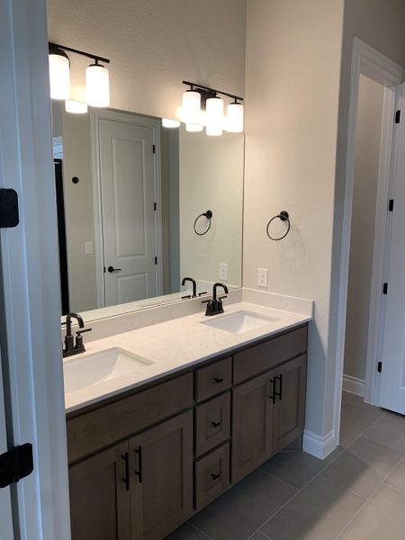 Contemporary bathroom with dual sinks, sleek black fixtures, wood cabinetry, and elegant lighting over a large mirror.