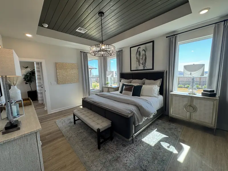 A sophisticated bedroom with elegant bedding, a stylish chandelier, and large windows letting in natural light.