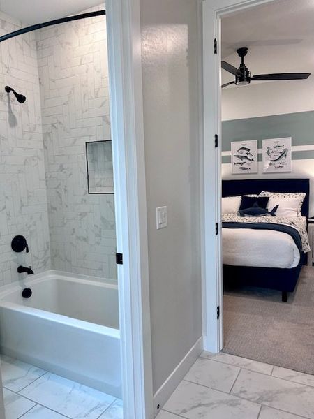 A chic bathroom with a tiled tub leads to a cozy bedroom featuring modern decor and stylish wall art.