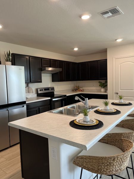 A modern kitchen with dark cabinets, a sleek island, stainless steel appliances, and stylish bar seating.