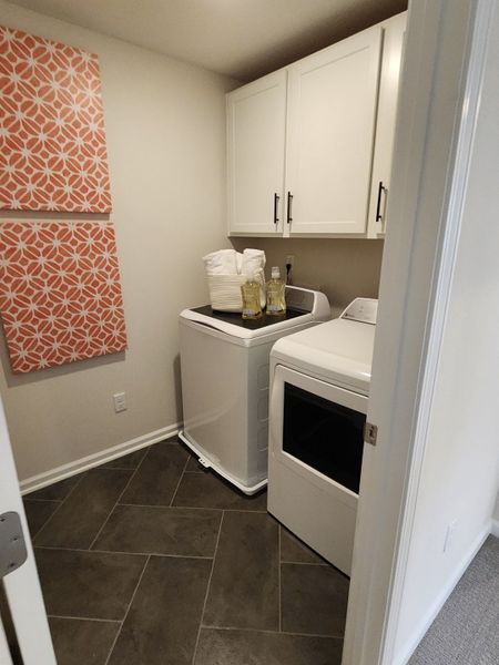 A cozy laundry room with sleek tile flooring, white cabinetry, and vibrant wall art for a modern touch.