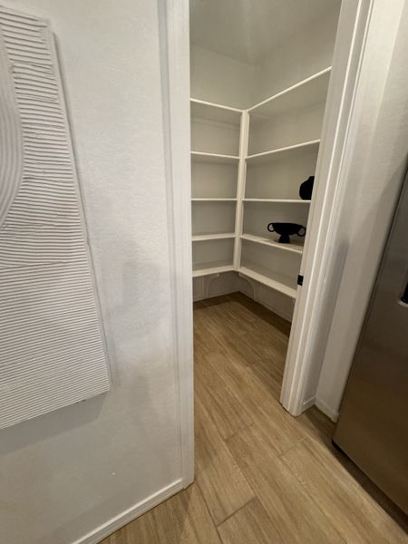A spacious walk-in pantry with sleek wood flooring and ample shelving for organized storage.