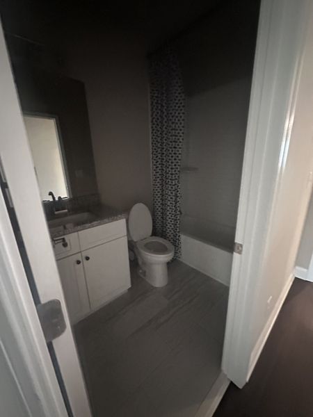 A compact bathroom featuring a white vanity, bathtub with a patterned curtain, and sleek modern flooring. A compact bathroom featuring a white vanity, bathtub with a patterned curtain, and sleek modern flooring.