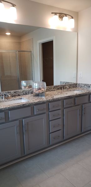 A modern bathroom with dual sinks, sleek gray cabinetry, granite countertops, and elegant lighting fixtures.