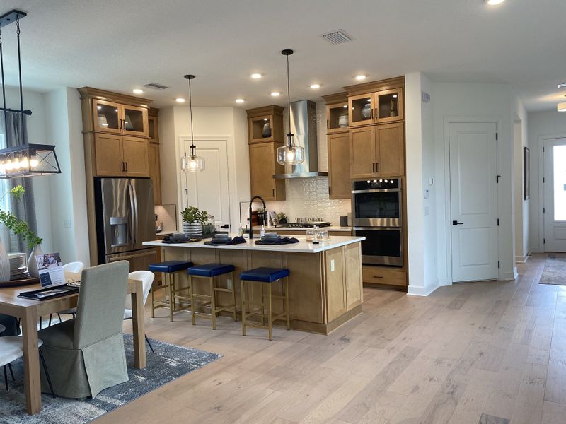 A modern kitchen with wooden cabinets, sleek appliances, an island with blue stools, and elegant lighting.