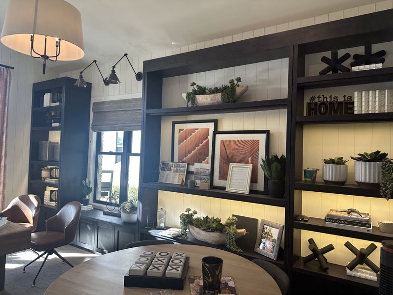 A cozy home office with dark wood shelving, plush leather chairs, and stylish decor accents on cream-paneled walls.