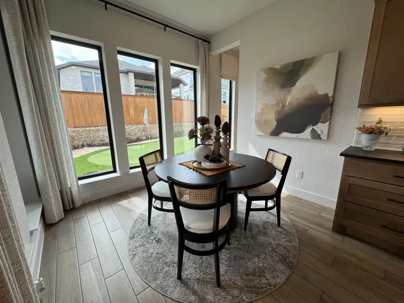 A cozy dining nook with large windows, wooden floors, a round table, and modern art creates an inviting, elegant space.