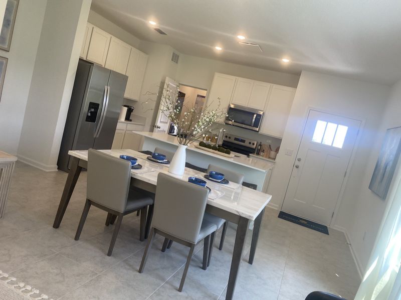 Modern kitchen and dining area with sleek appliances, a marble-topped table, and elegant gray chairs.