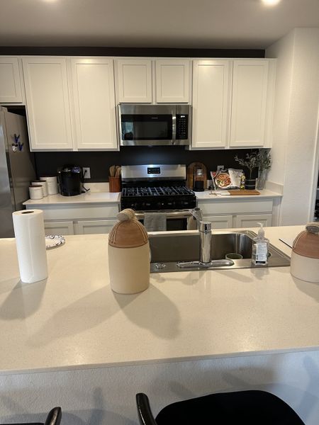 A modern kitchen featuring sleek white cabinets, stainless steel appliances, and a spacious countertop with a double sink. A modern kitchen featuring sleek white cabinets, stainless steel appliances, and a spacious countertop with a double sink.