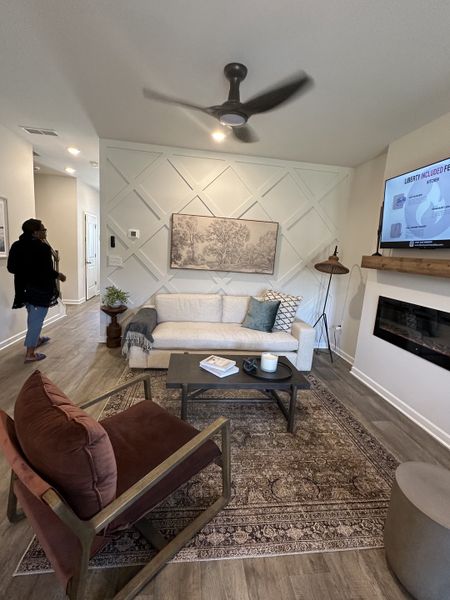 A cozy living room featuring a textured accent wall, modern ceiling fan, and elegant decor with plush seating.