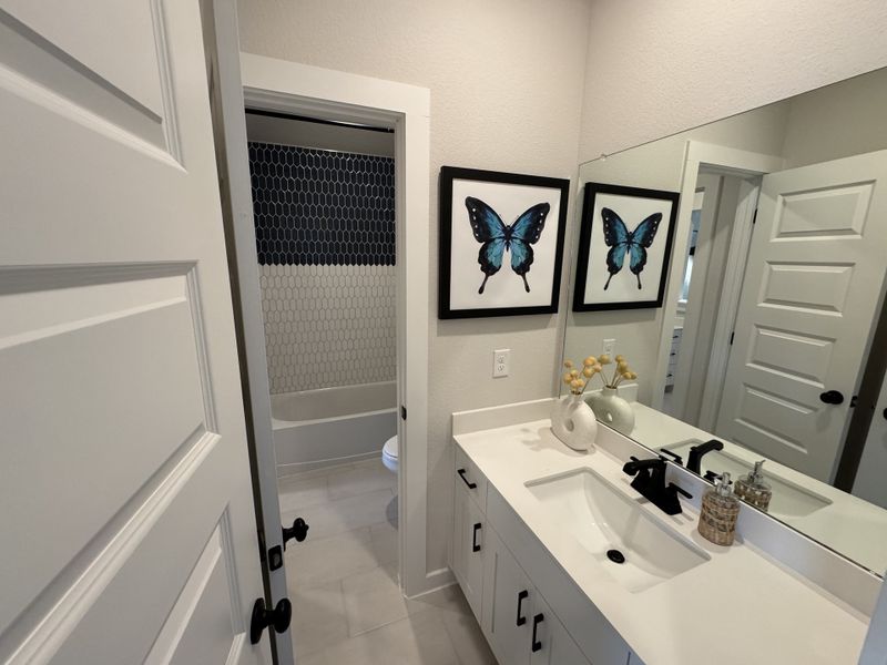 A modern bathroom with sleek white countertops, black fixtures, and butterfly artwork, featuring a stylish tub area.