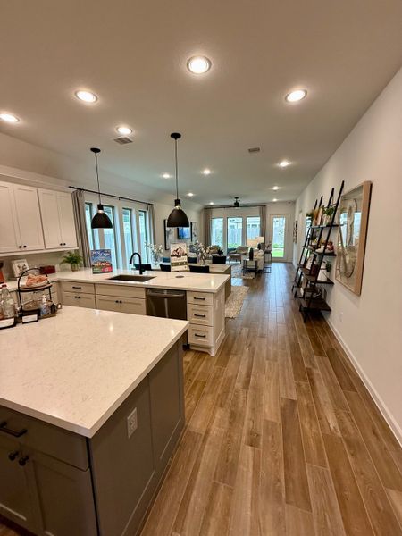 A modern kitchen and living area featuring wood floors, pendant lights, and a spacious island with pristine countertops.