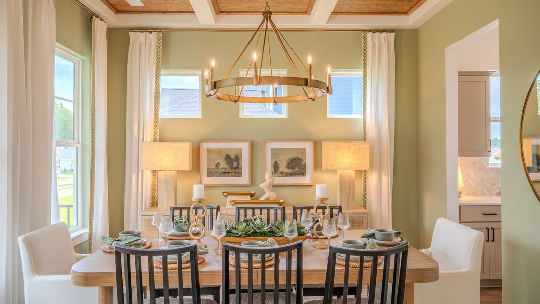Dining area with coffered ceiling, access to kitchen, and bright natural lighting from windows Dining area with coffered ceiling, access to kitchen, and bright natural lighting from windows