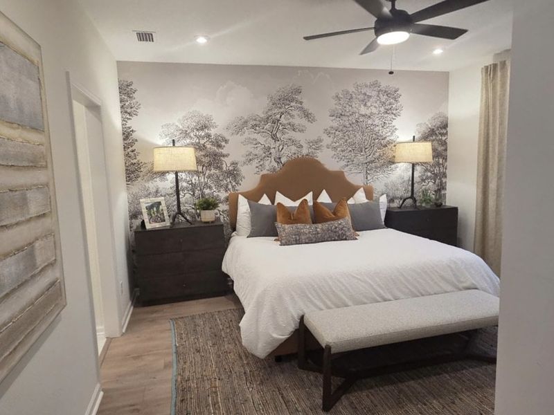 A cozy bedroom featuring a large bed with decorative cushions, nature-themed wallpaper, and elegant bedside lamps.