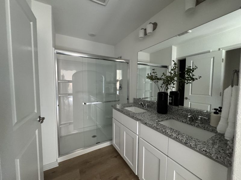 A modern bathroom featuring a dual-sink granite vanity, elegant lighting, and a sleek glass shower enclosure. A modern bathroom featuring a dual-sink granite vanity, elegant lighting, and a sleek glass shower enclosure.