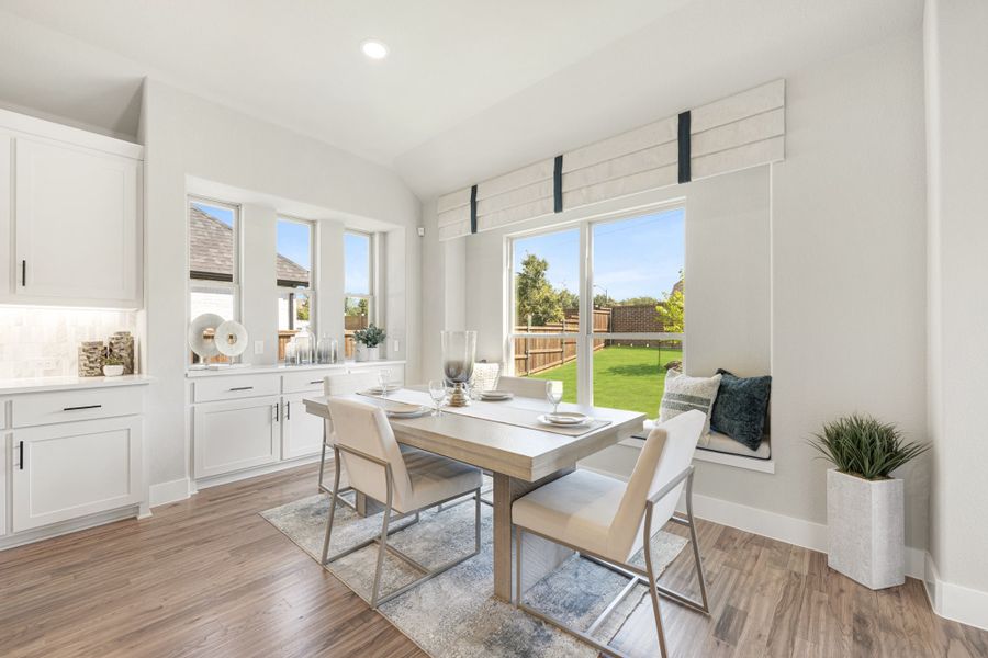 Bright dining area with wood floors, window seat, and large windows overlooking a backyard