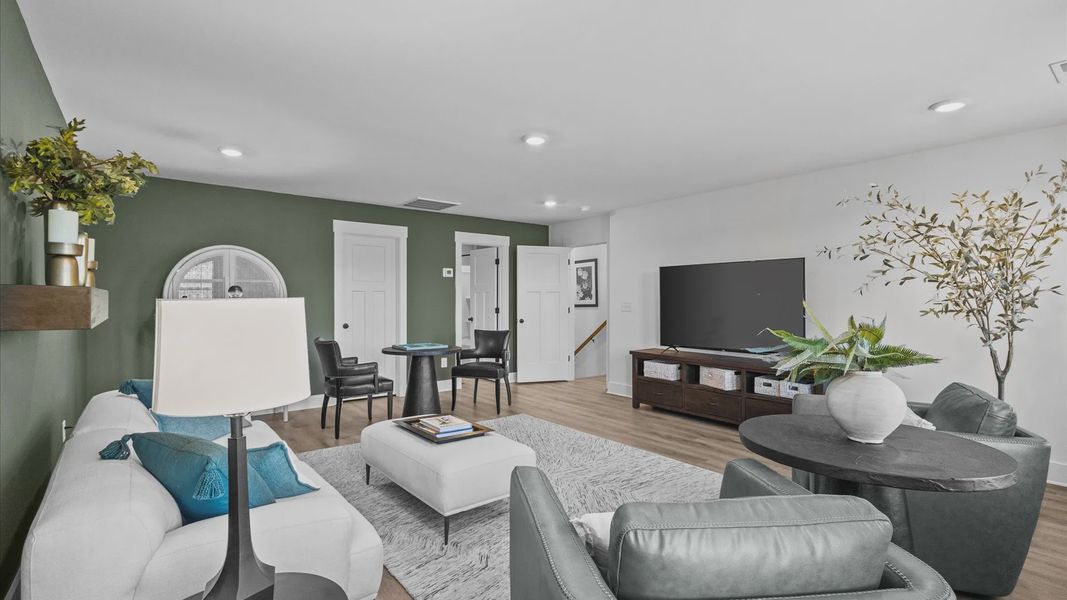 New two-story home with green accent wall, hardwood flooring, and overhead lighting at Wells Crossing by DRB Homes