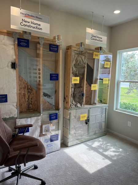 A comparative display of new vs. used home construction materials, featuring detailed cross-sections and comfortable office seating.