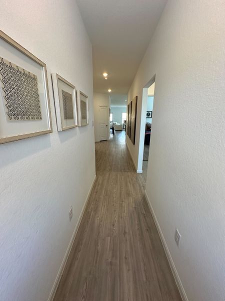 A bright hallway with wood flooring and framed art leads to a cozy living area, creating a welcoming atmosphere.