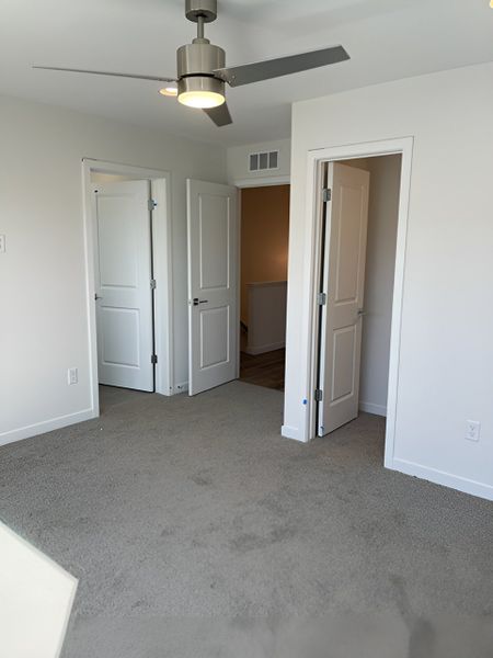A serene primary bedroom with plush carpeting, a ceiling fan, and abundant natural light.