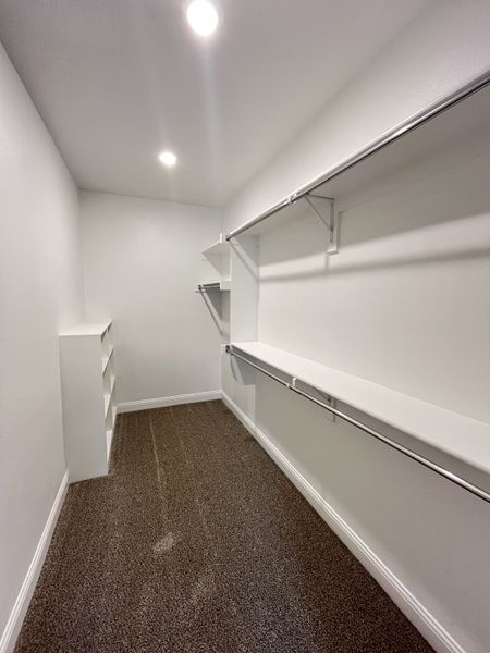 A spacious walk-in closet with ample shelving, sturdy hanging rods, and plush carpeting.