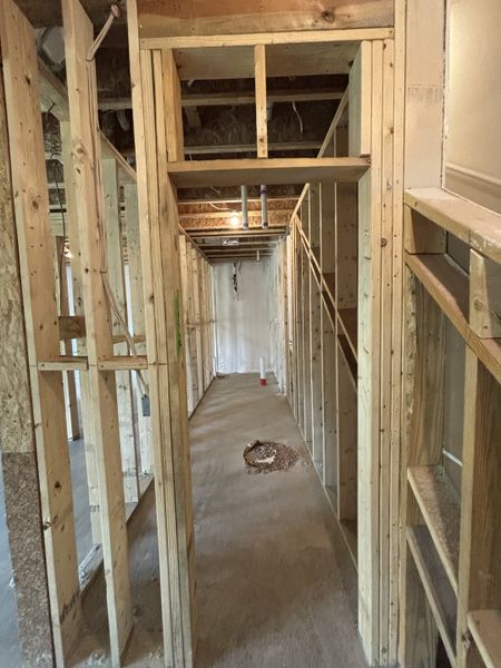A house under construction with exposed wooden framing and concrete flooring.