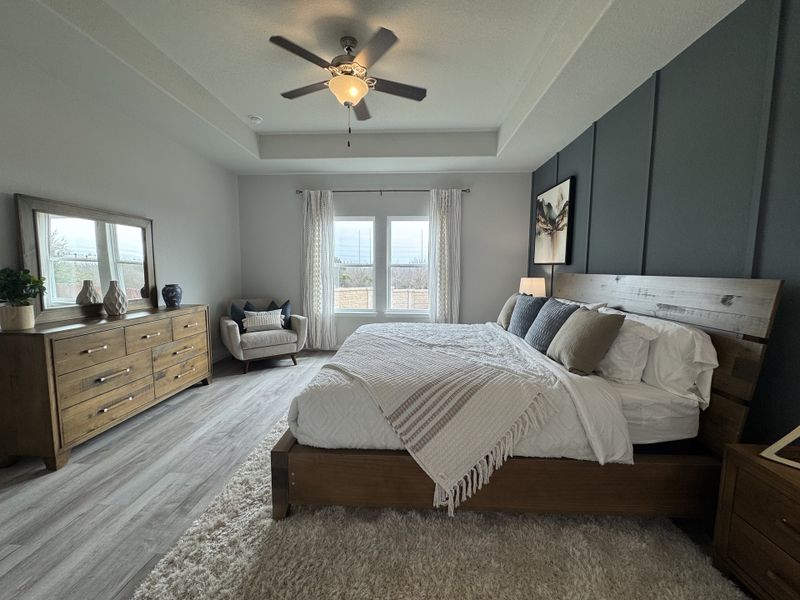 A spacious bedroom with wood flooring, textured accent wall, and cozy decor in neutral tones.