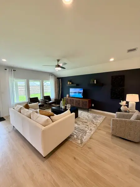 A cozy living room with a cream sofa, dark feature wall, modern fan, and large windows brightening the space.