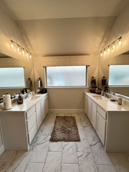 A luxurious bathroom with marble floors, dual vanities, and chic lighting, offering a serene and elegant ambiance.