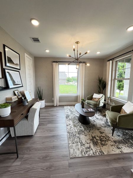 A modern sitting room featuring hardwood floors, a sleek chandelier, and stylish furnishings in an elegant, cozy setting.
