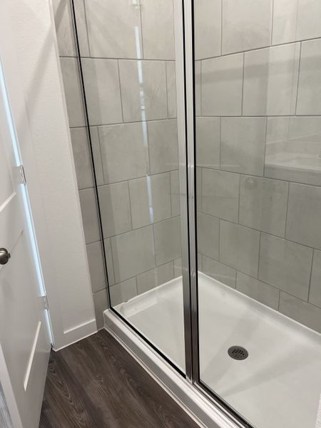 A sleek shower with glossy tiles and a chrome-framed glass door, set against modern wood flooring. A sleek shower with glossy tiles and a chrome-framed glass door, set against modern wood flooring.