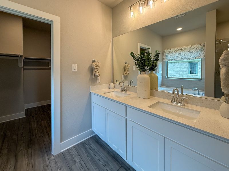 A sleek bathroom featuring a dual sink vanity, large mirror, and soft lighting, leading to a spacious walk-in closet.
