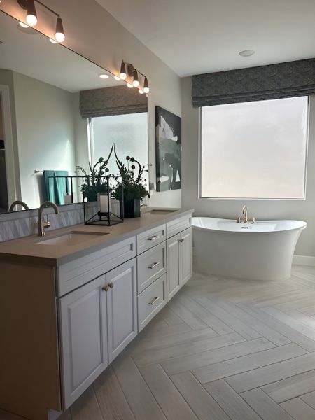 A luxurious bathroom featuring a freestanding tub, double vanity with gold accents, and a large frosted window.