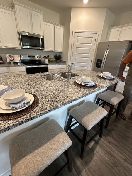A modern kitchen with granite countertops, a sleek island with seating, and stainless steel appliances.