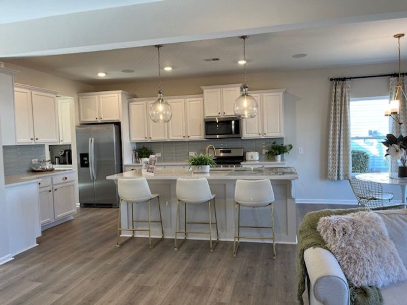 A modern kitchen with sleek white cabinets, a spacious island, stylish pendant lights, and cozy dining area.