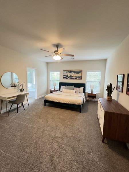 A cozy bedroom with plush carpeting, a modern bed, stylish artwork, and an elegant workspace with a round mirror.