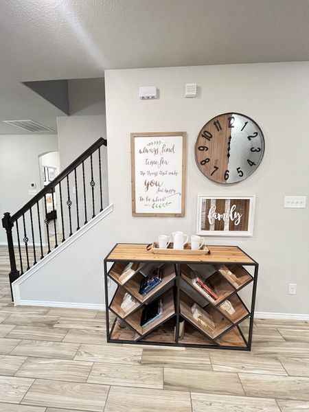 Stylish hallway with geometric shelving, modern clock, and motivational wall art. Wood floors and elegant stair railing.
