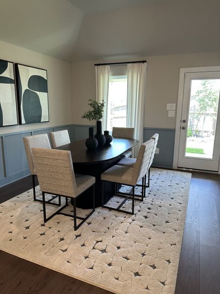 A modern dining room featuring a sleek oval table, upholstered chairs, abstract art, and natural light from a large window. A modern dining room featuring a sleek oval table, upholstered chairs, abstract art, and natural light from a large window.