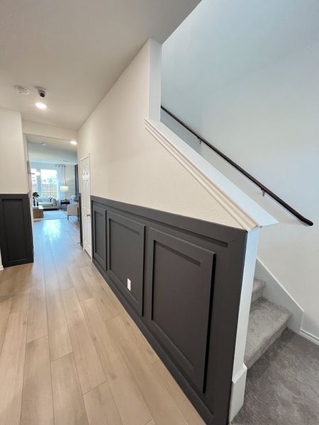 A modern hallway with sleek wood flooring, accented black paneling, and stairs leading to a bright living area. A modern hallway with sleek wood flooring, accented black paneling, and stairs leading to a bright living area.